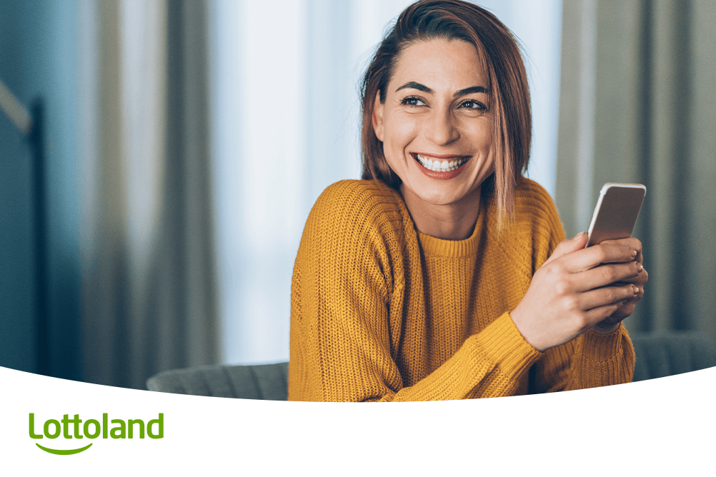 Fröhliche Frau informiert sich lächelnd per Smartphone bei Lottoland über die besten Lottozahlen und erfährt Vor- und Nachteile beliebter Zahlenkombinationen für bessere Gewinnchancen.